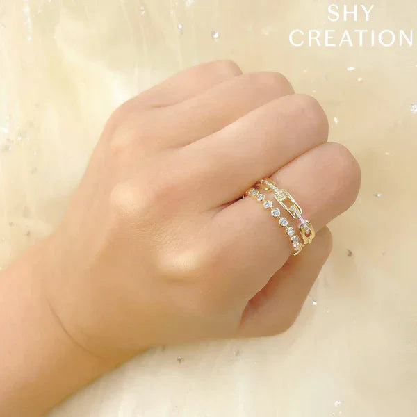 Hand wearing a gold ring with small stones on a light background, branded 'SHY CREATION'.