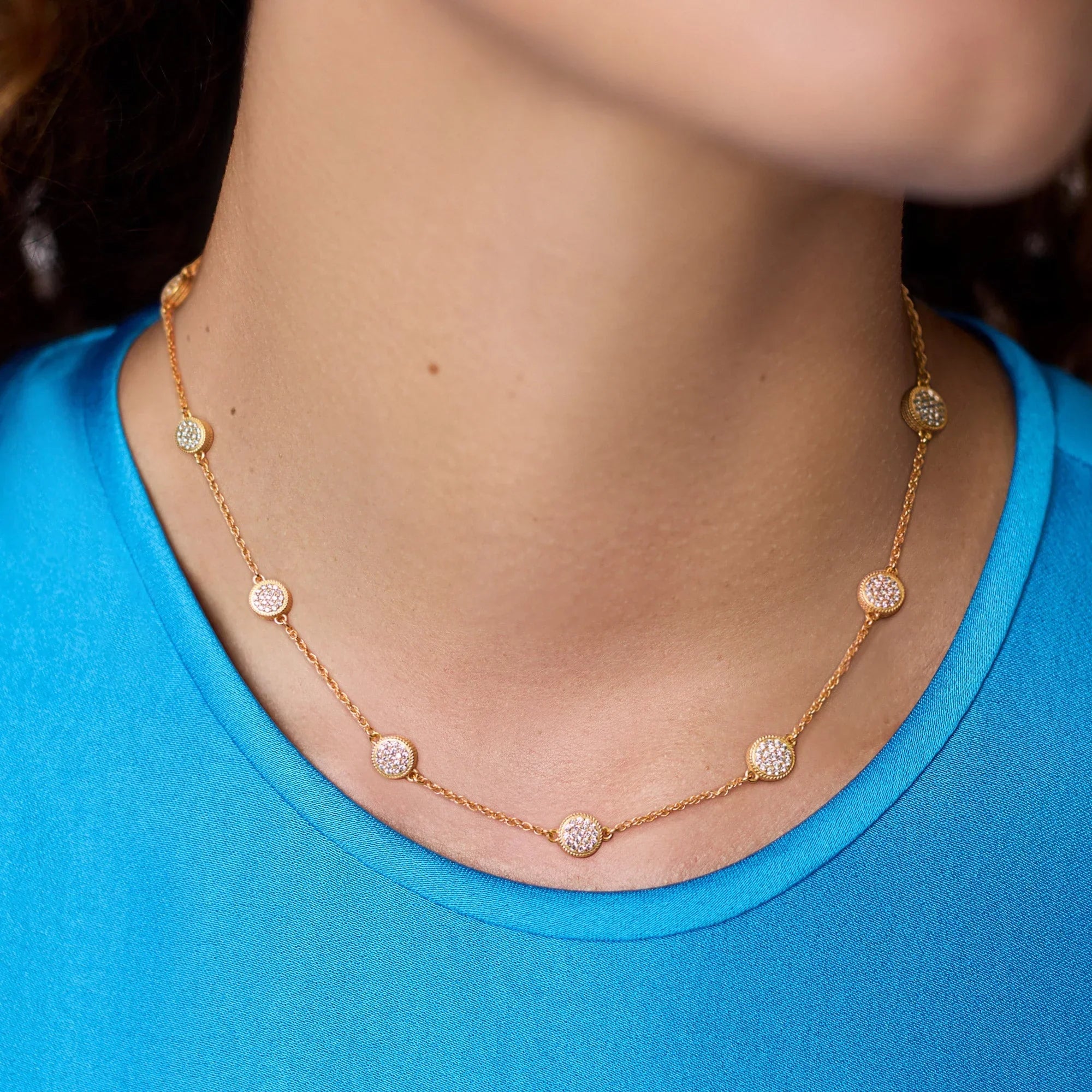 Gold necklace with diamond-like stones worn by a person in a blue shirt